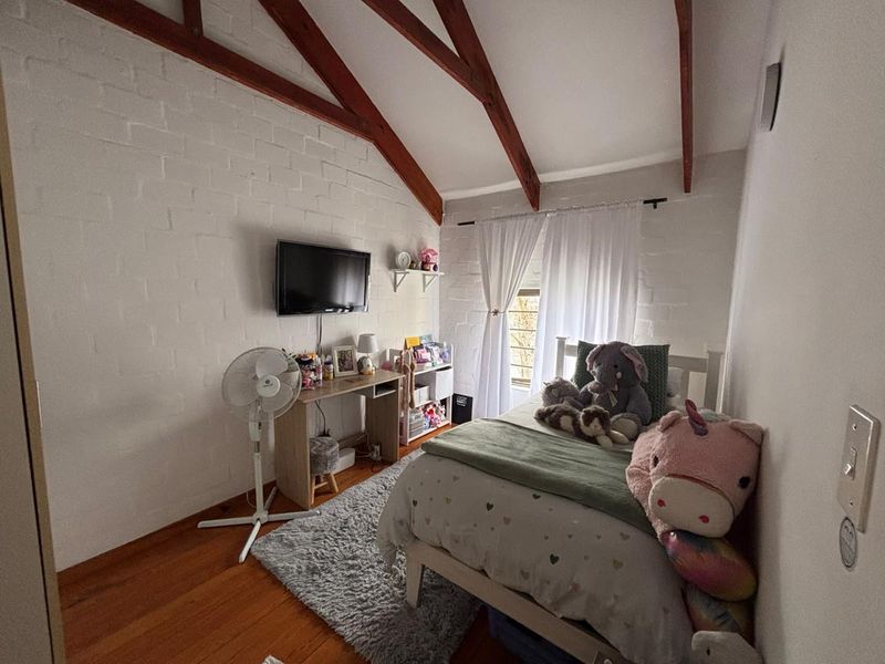 A cozy bedroom featuring exposed timber rafters, painted brick walls, and warm timber flooring, creating a charming and character-filled living space.