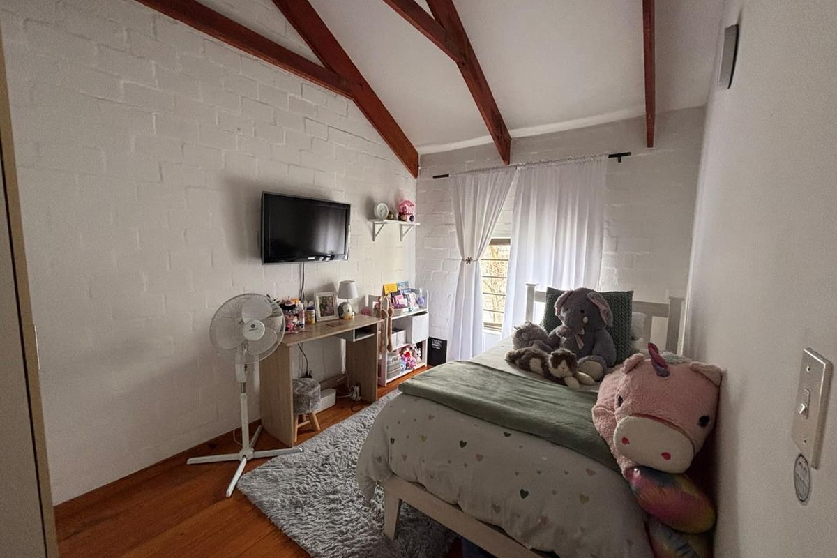 A cozy bedroom featuring exposed timber rafters, painted brick walls, and warm timber flooring, creating a charming and character-filled living space.