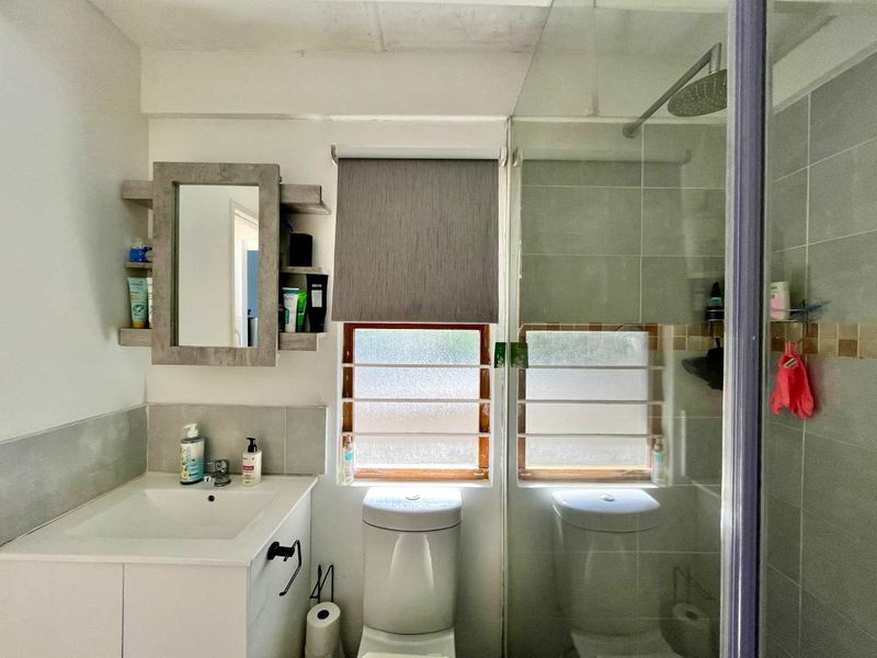A functional bathroom featuring a vanity cabinet, toilet, and a glass-enclosed shower with tiled walls and natural light from the windows.