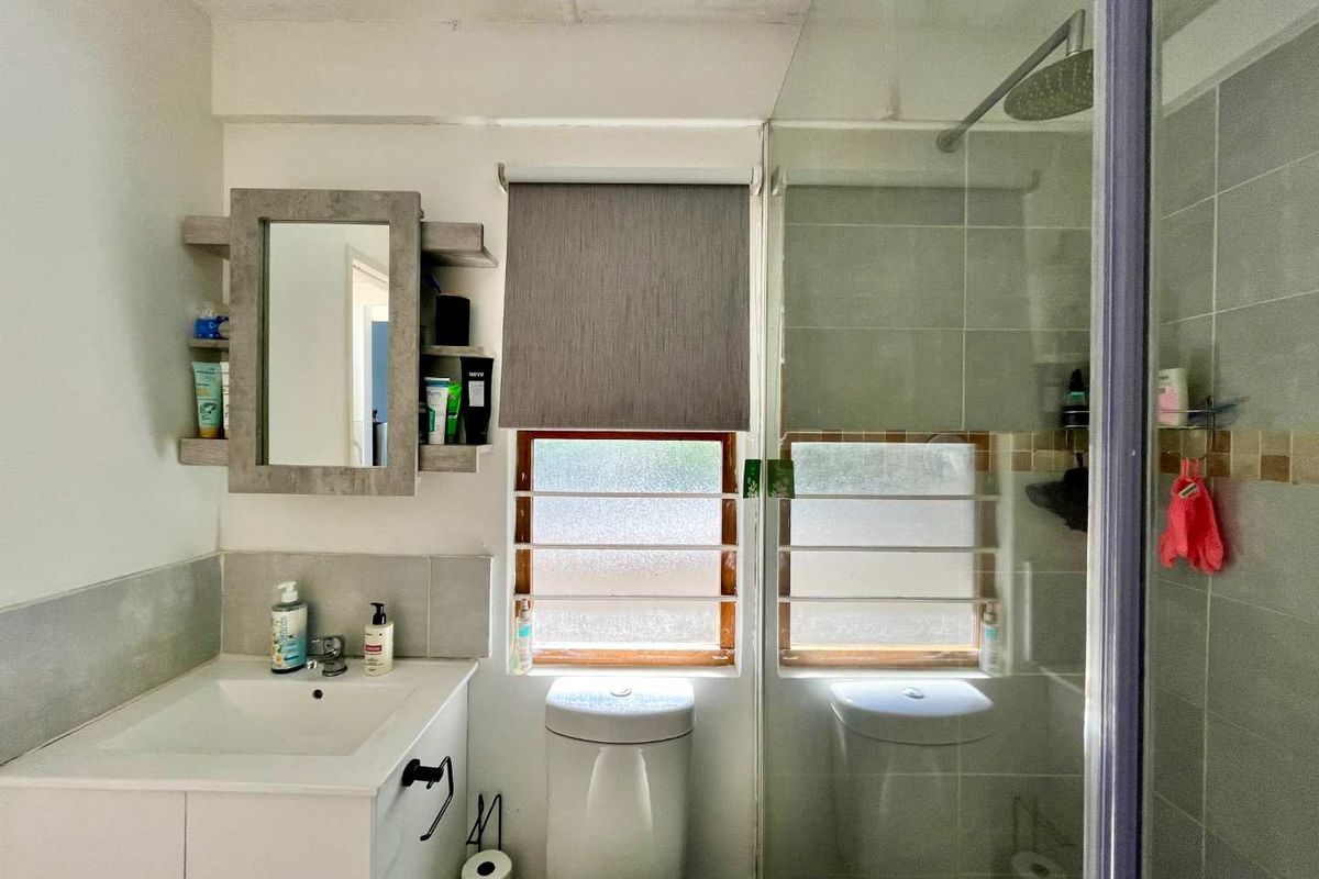 A functional bathroom featuring a vanity cabinet, toilet, and a glass-enclosed shower with tiled walls and natural light from the windows.