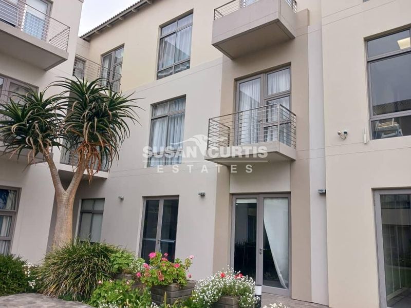 Rear elevation of a modern retirement village apartment building featuring balconies with stainless steel balustrades and aluminium framed windows and doors.