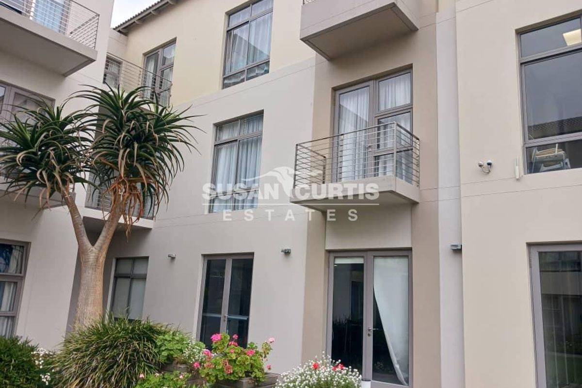 Rear elevation of a modern retirement village apartment building featuring balconies with stainless steel balustrades and aluminium framed windows and doors.