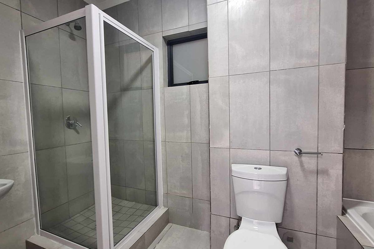A modern, neutral-toned bathroom featuring a glass-enclosed shower, a bathtub, a pedestal basin, and a toilet with full-height wall tiling.
