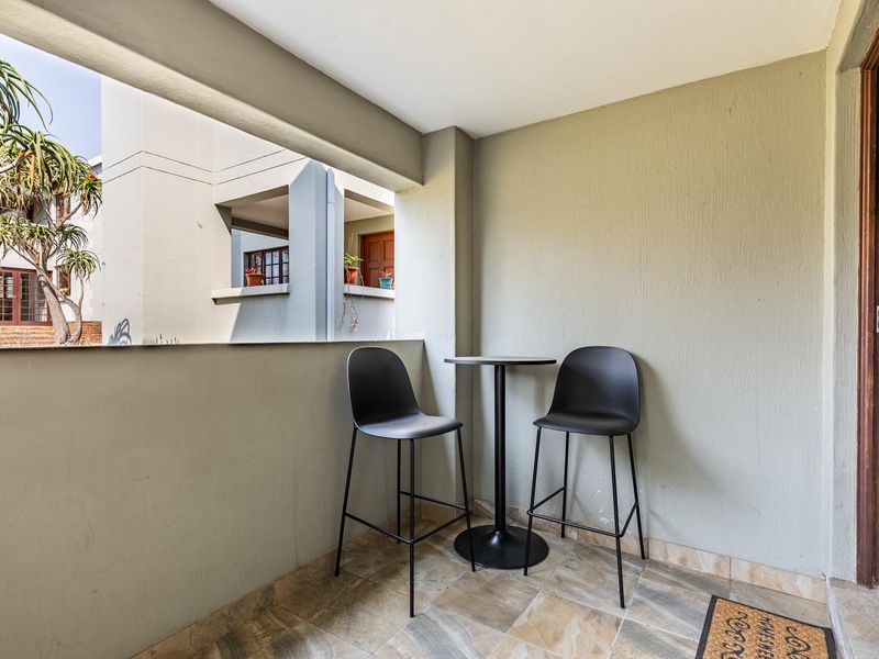 A compact covered balcony featuring tiled flooring and a solid balustrade, offering a functional outdoor space for relaxation.