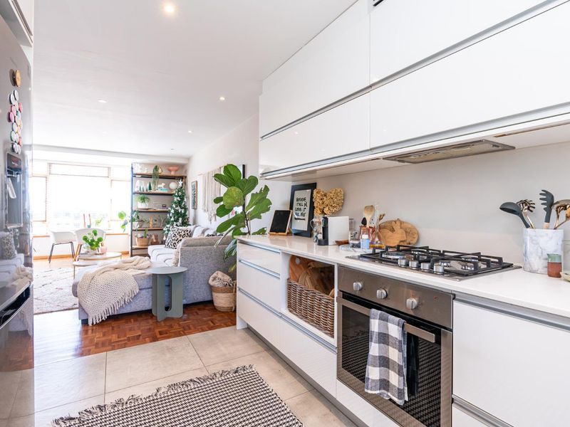 Modern open-plan kitchen and living area featuring sleek white cabinetry, integrated gas hob, built-in oven, and a blend of parquet and tiled flooring.