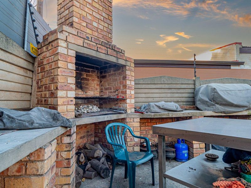 Outdoor patio area featuring a built-in brick braai, concrete prep surfaces, and perimeter wall with electric fencing.