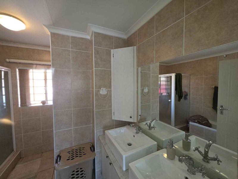 A functional bathroom featuring a double vanity with built-in cabinetry, tiled walls, and a separate shower enclosure.