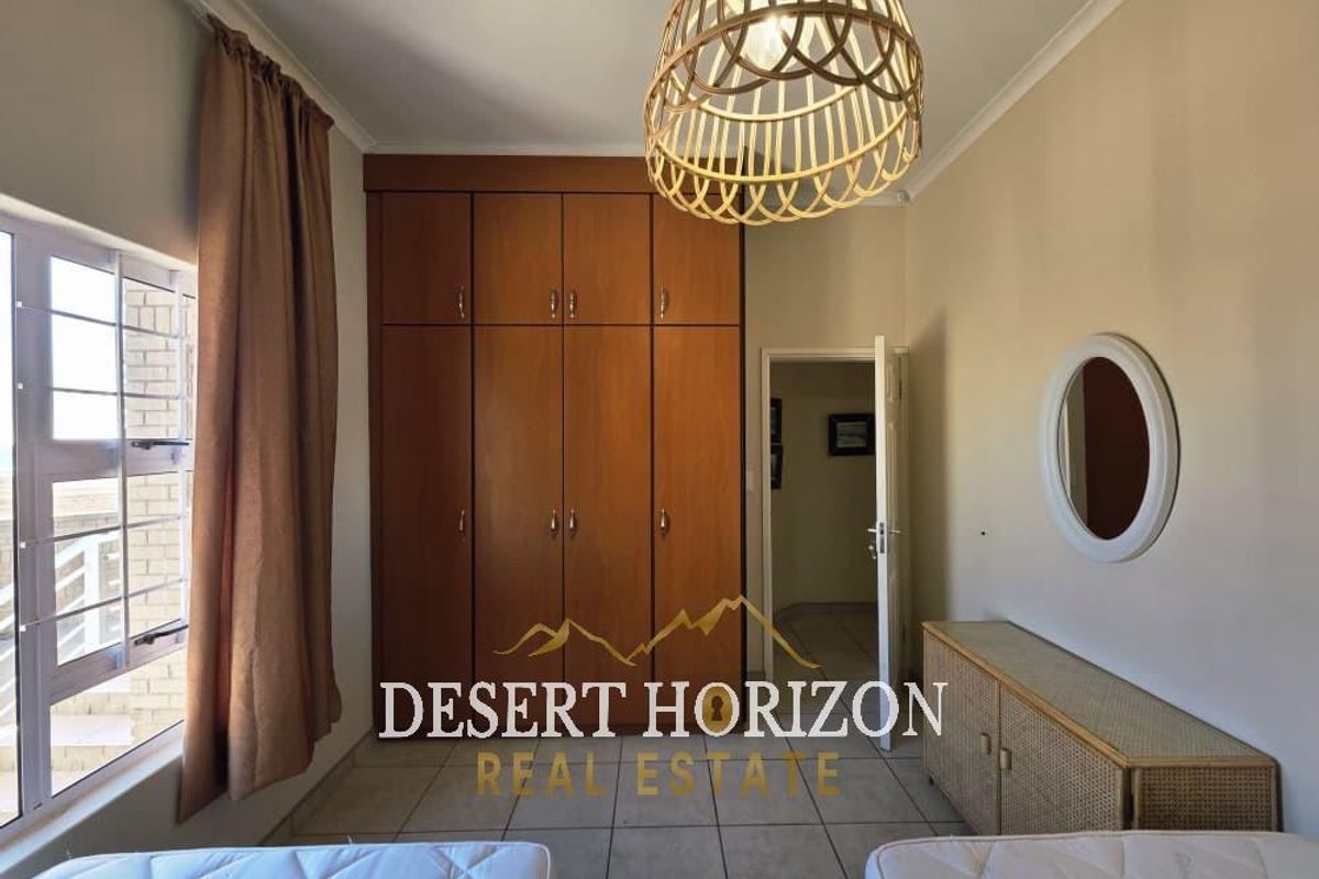A bedroom featuring built-in wooden cupboards, tiled flooring, and a window with natural light.