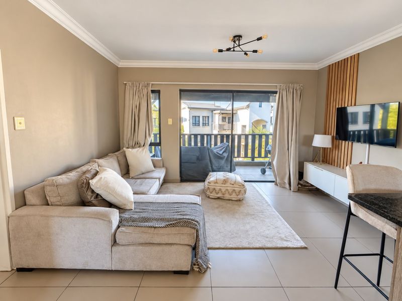 A bright and modern living room featuring tiled floors, crown molding, a decorative wooden slat wall, and large sliding doors leading to a balcony.
