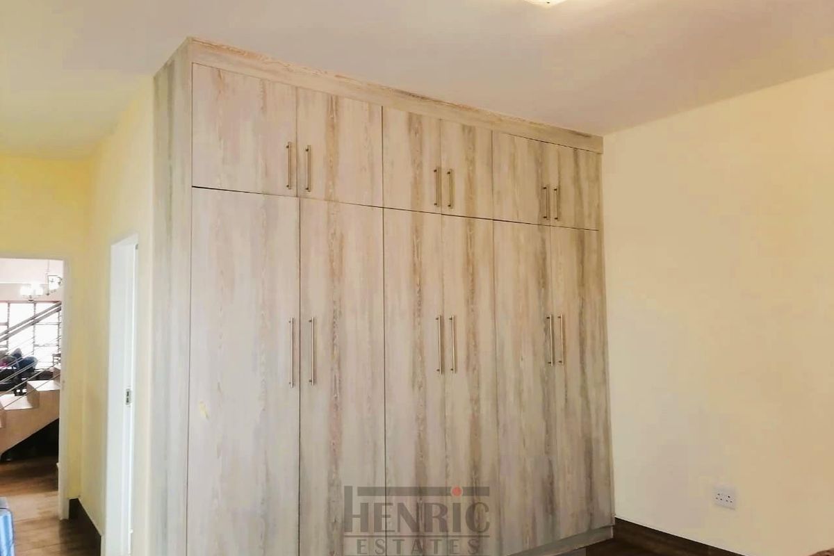 A bright bedroom featuring modern wood-finish built-in cupboards and laminate flooring, offering ample storage space.