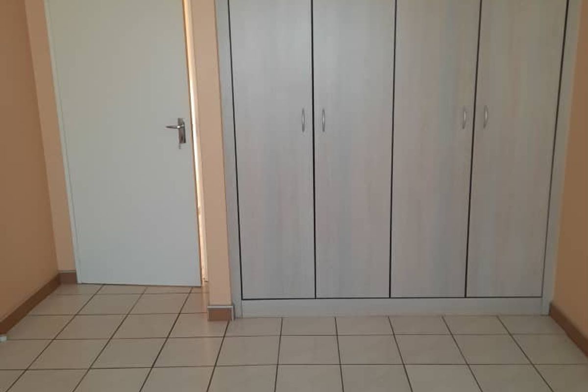 A clean, empty bedroom featuring neutral tiled flooring and floor-to-ceiling built-in cupboards with light wood-grain finish.