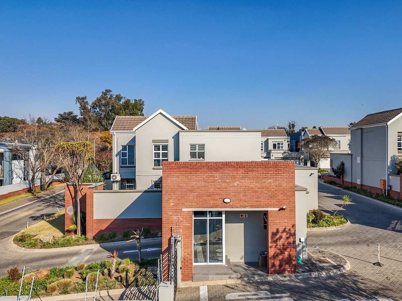 Aerial view of the cluster property entrance featuring a brick facade, paved driveway, and secure perimeter fencing within a well-maintained residential estate.