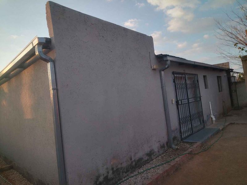 Rear exterior view of the property featuring plastered walls, metal guttering, and a security gate entrance.