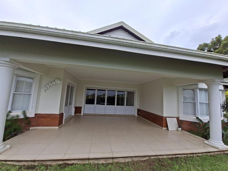 A spacious covered patio featuring tiled flooring, structural columns, and large sliding glass doors providing access to the interior living space.
