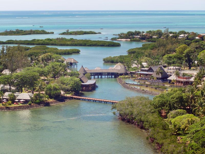 An expansive aerial view of a coastal estate featuring lush tropical landscaping, interconnected waterways, and traditional thatched-roof structures.