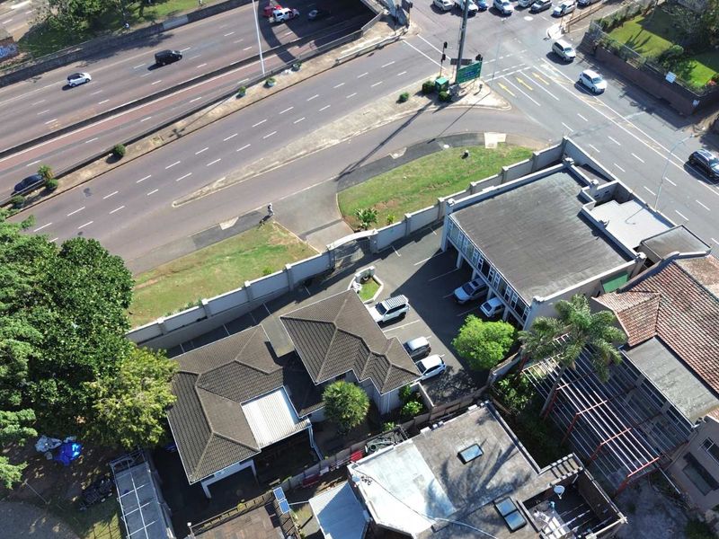 Aerial view of the commercial property showing the building layout, tiled roof structures, paved parking area, and perimeter walling adjacent to the main road.