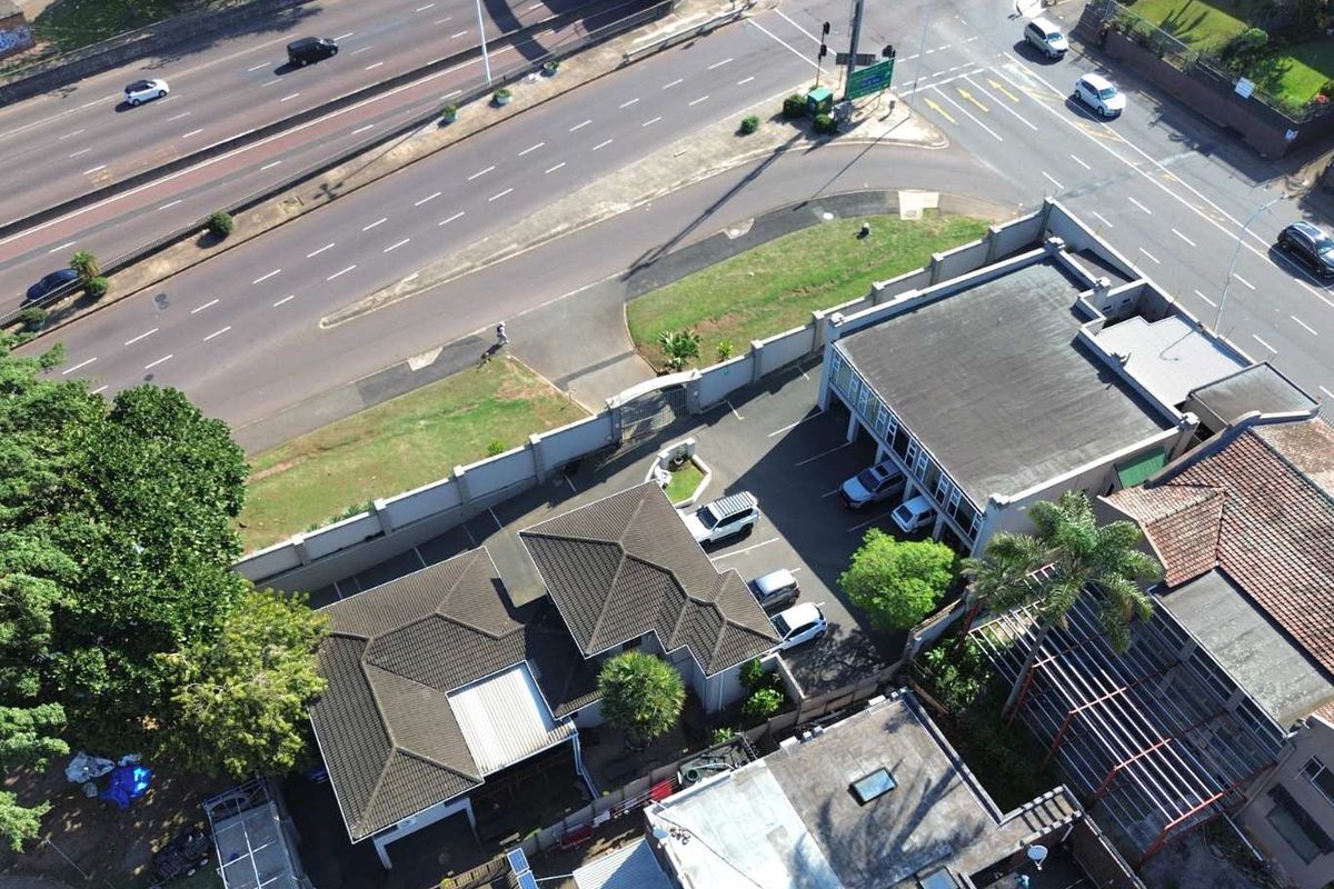 Aerial view of the commercial property showing the building layout, tiled roof structures, paved parking area, and perimeter walling adjacent to the main road.
