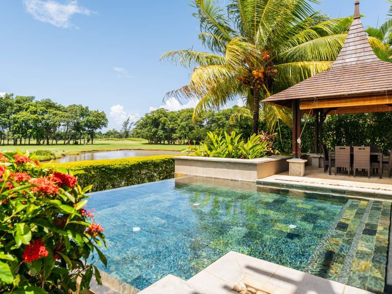A private infinity pool overlooking a lush golf course, featuring a covered gazebo and tropical landscaping.