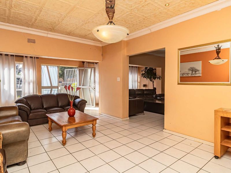 Spacious living area featuring tiled flooring, a textured ceiling, and large aluminium windows, offering a functional layout with potential for modern updates.
