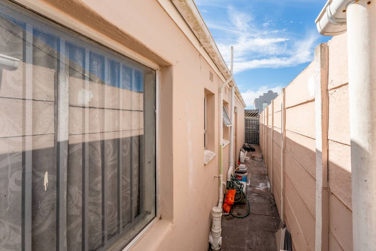 A narrow side passage of the house featuring concrete paving, exterior wall access, and boundary walling.