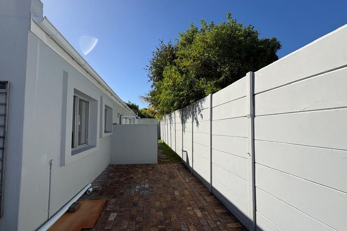 A side exterior walkway featuring paved flooring, a high boundary wall, and exterior wall-mounted lighting.