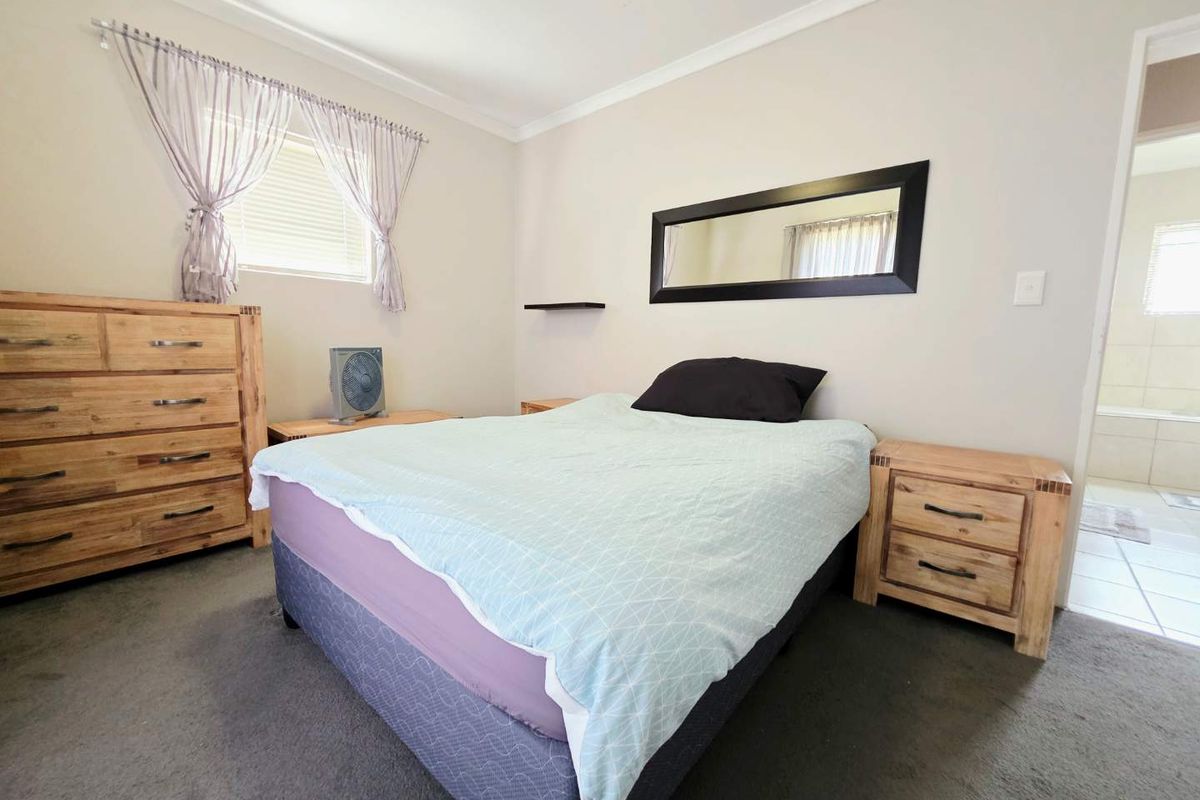 A well-lit bedroom featuring neutral walls, carpeted flooring, and a doorway leading to an adjoining bathroom.