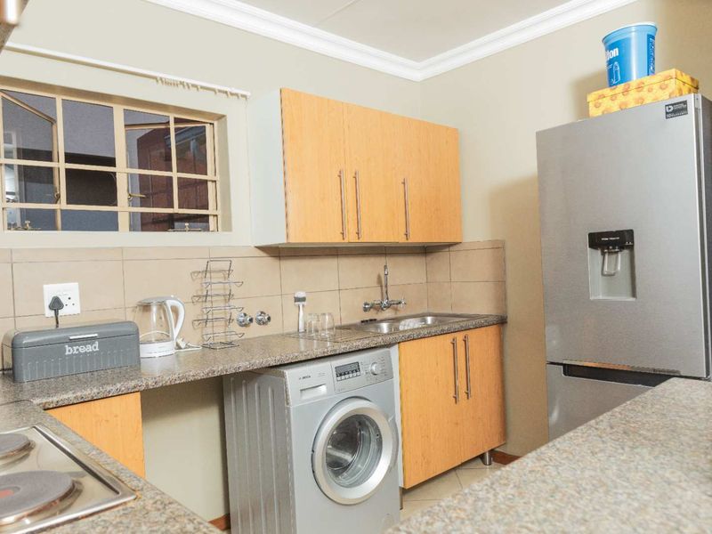A functional kitchen featuring wooden cabinetry, granite countertops, a tiled backsplash, and integrated space for laundry appliances.
