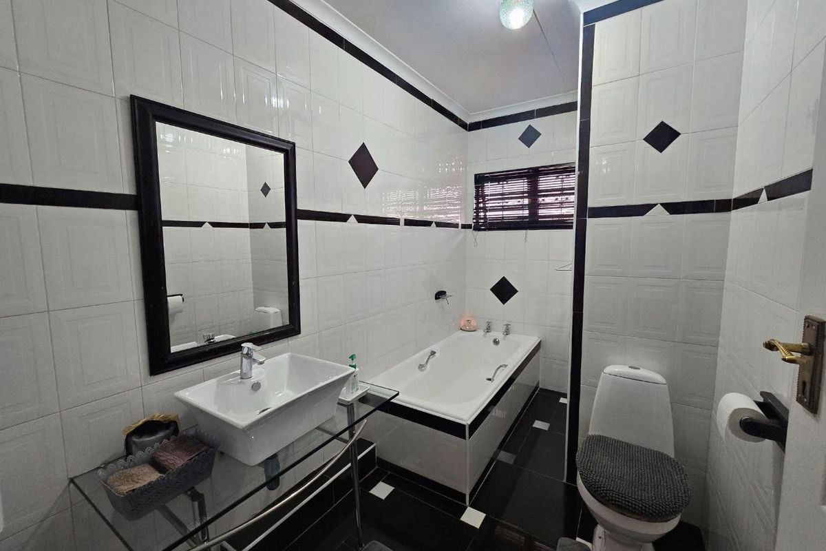 A functional bathroom featuring a built-in bathtub, wall-mounted basin, and toilet, finished with classic black and white wall and floor tiling.