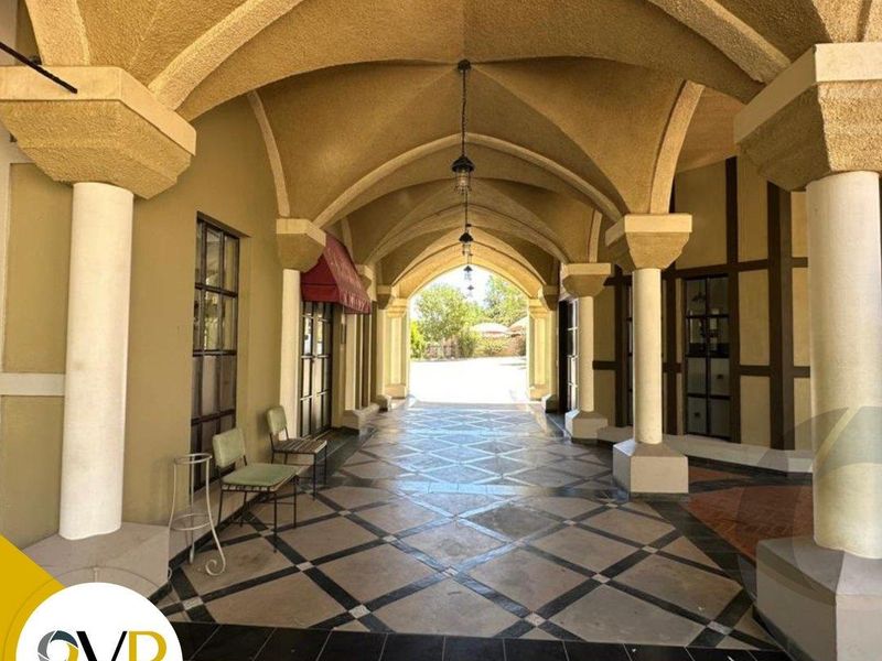 A covered outdoor walkway featuring elegant vaulted ceilings, stone columns, and decorative tiled flooring, providing a sophisticated architectural transition space.