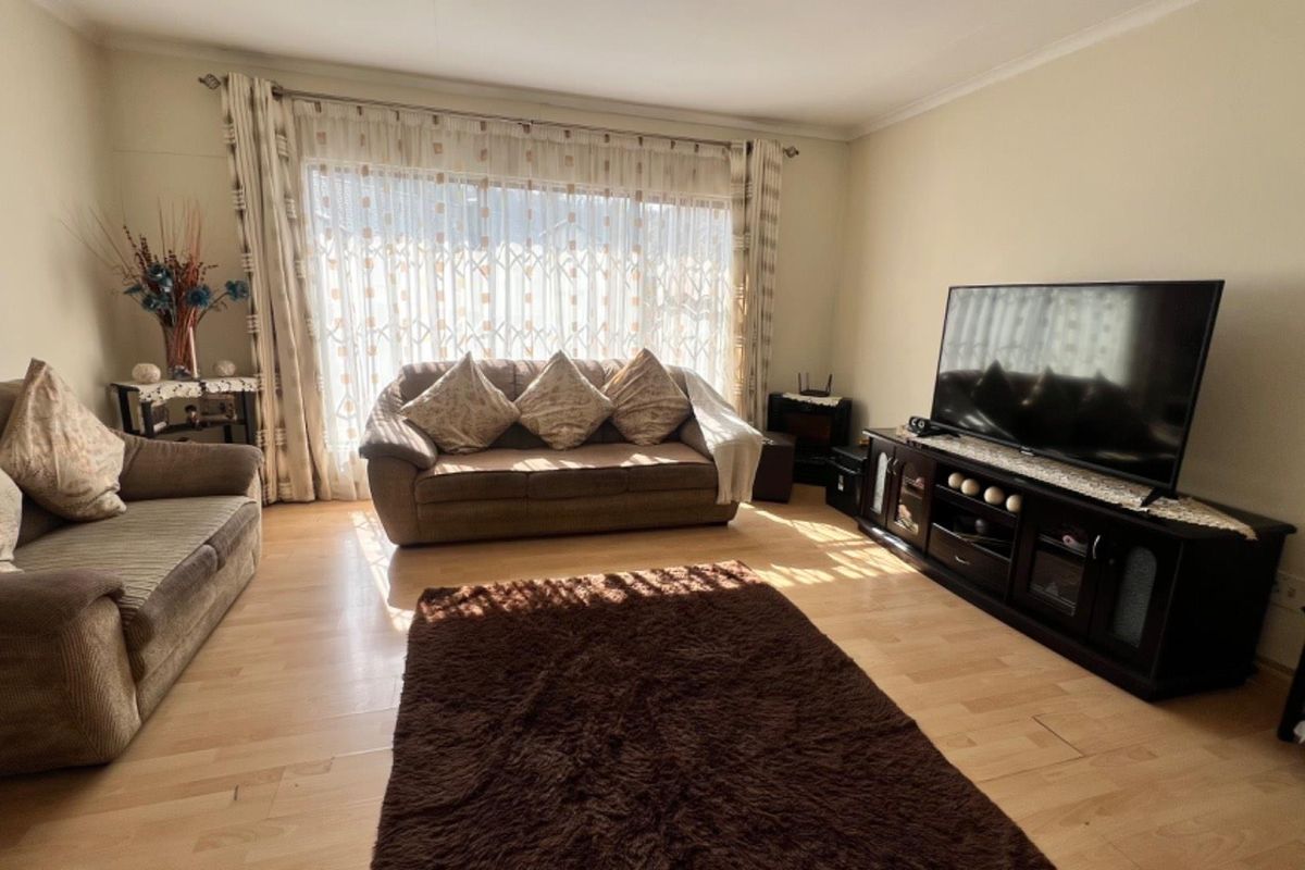 A comfortable living room featuring light-toned laminate flooring and large windows with curtains, providing a bright and inviting space for relaxation.