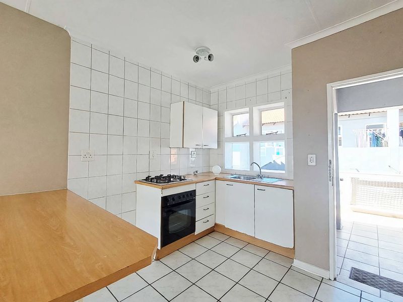 A functional kitchen featuring built-in cabinetry, a gas hob, an oven, and a breakfast counter, with direct access to an outdoor area.