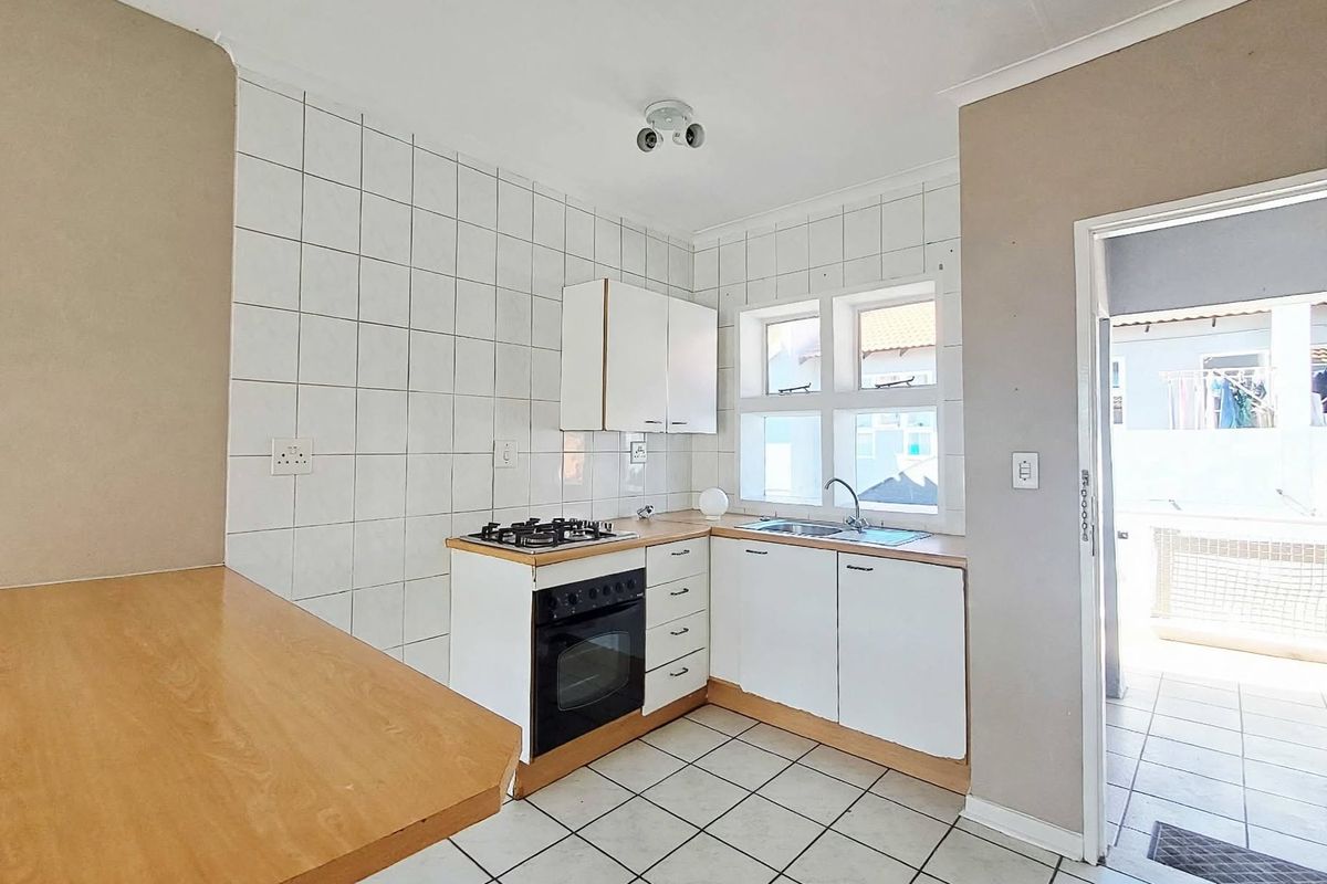 A functional kitchen featuring built-in cabinetry, a gas hob, an oven, and a breakfast counter, with direct access to an outdoor area.