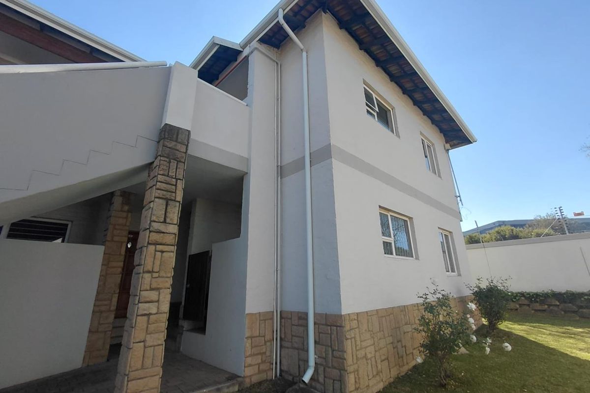 Rear elevation of a two-story apartment building featuring stone cladding accents, external staircase, and well-maintained exterior walls.