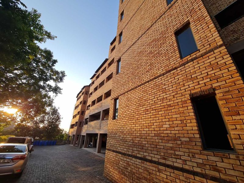 Exterior view of a multi-story apartment building featuring a face brick facade and a paved driveway with covered parking.