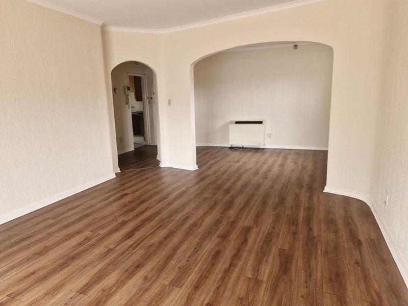 An empty, open-plan living area featuring laminate wood-look flooring, arched transitions between spaces, and a wall-mounted heater.
