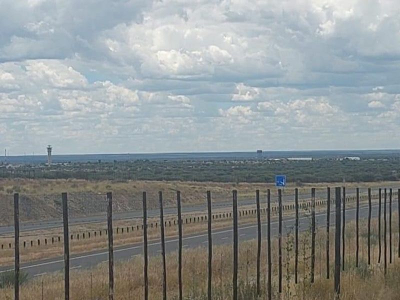 A wide-angle view of the agricultural land featuring perimeter fencing with a highway and distant landscape in the background.