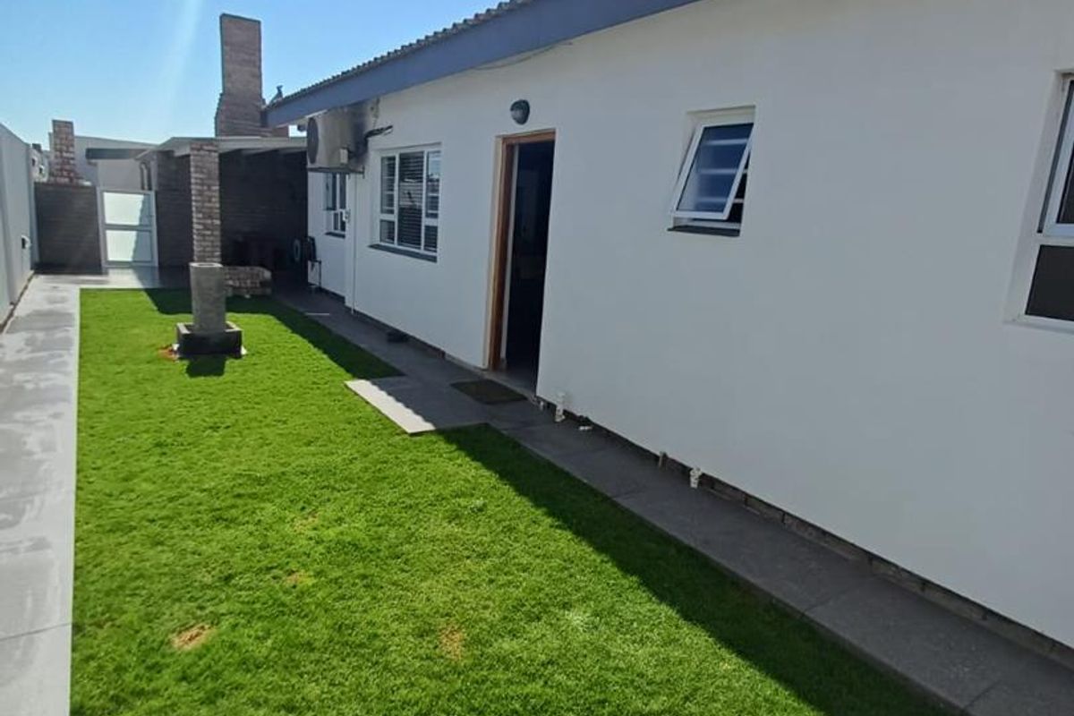 A view of the rear exterior of the house featuring a lawn, paved walkway, and a brick built-in braai area.