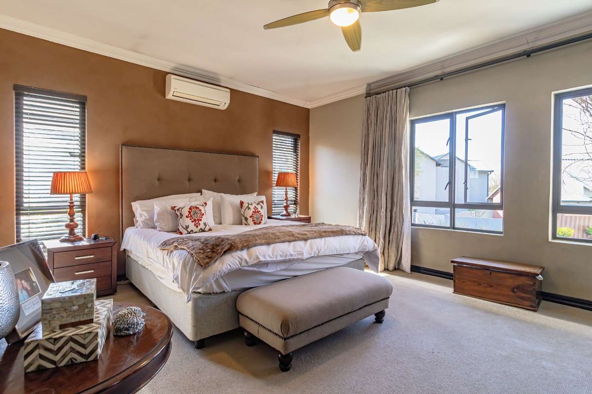 Spacious bedroom featuring neutral wall tones, carpeted flooring, a ceiling fan, and a wall-mounted air conditioning unit for climate control.