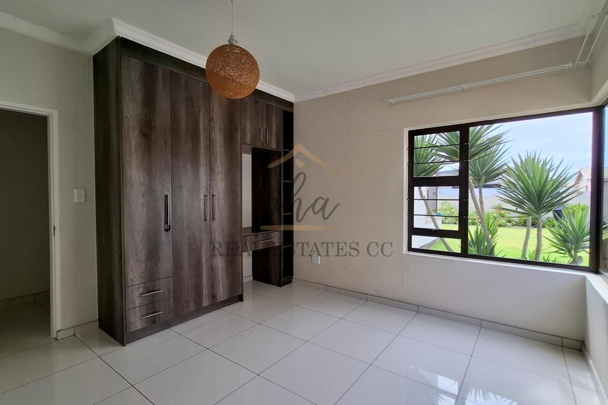 A bright bedroom featuring built-in dark wood cabinetry with an integrated desk, tiled flooring, and large windows overlooking the garden.
