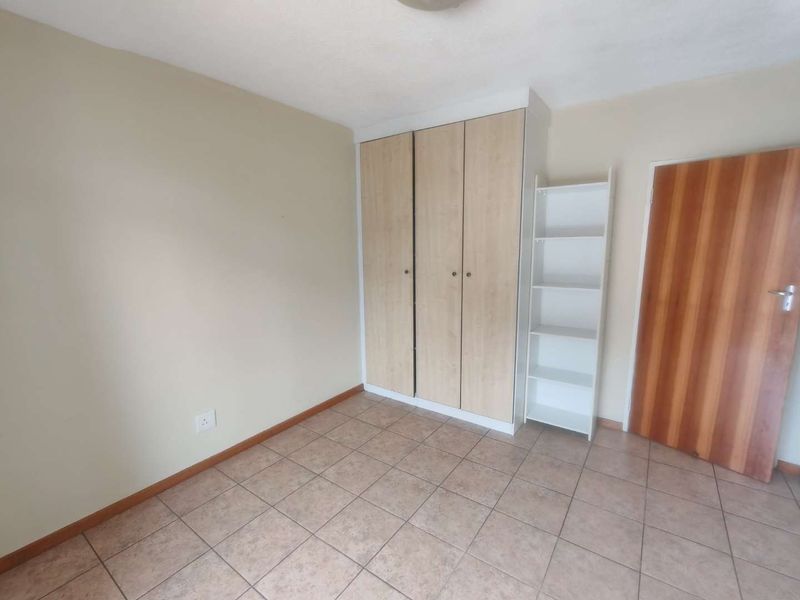 A clean, empty bedroom featuring neutral walls, tiled flooring, and a built-in wardrobe with light wood-finish doors.