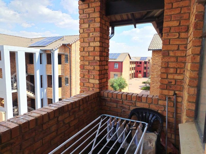 A covered balcony featuring exposed brick construction, overlooking the apartment complex courtyard with solar panels visible on surrounding roofs.
