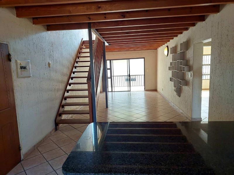 Open plan living area featuring exposed timber beams, tiled flooring, and a staircase leading to the upper level, with access to a balcony.