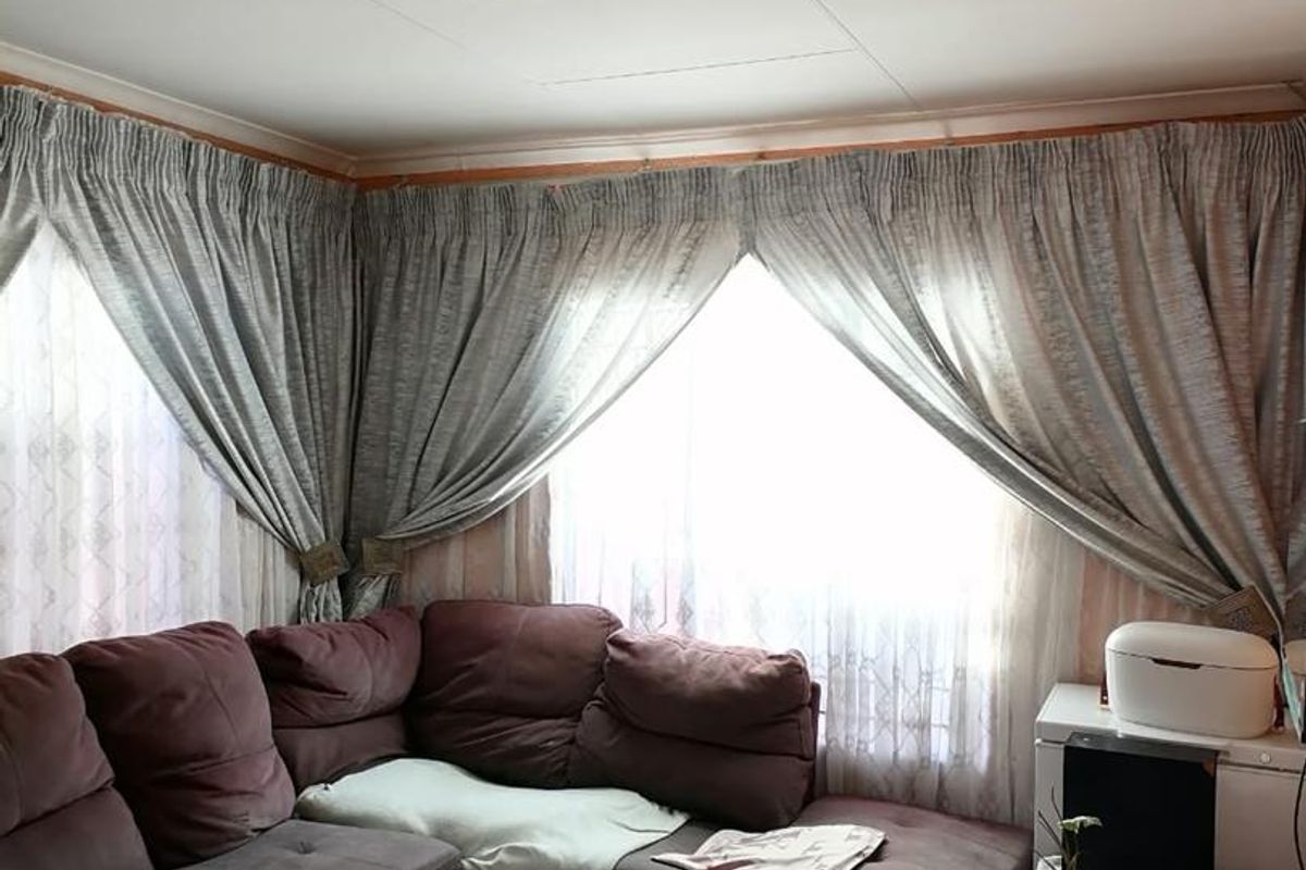 A living room featuring large windows with curtains and tiled flooring, providing a functional and comfortable space for relaxation.