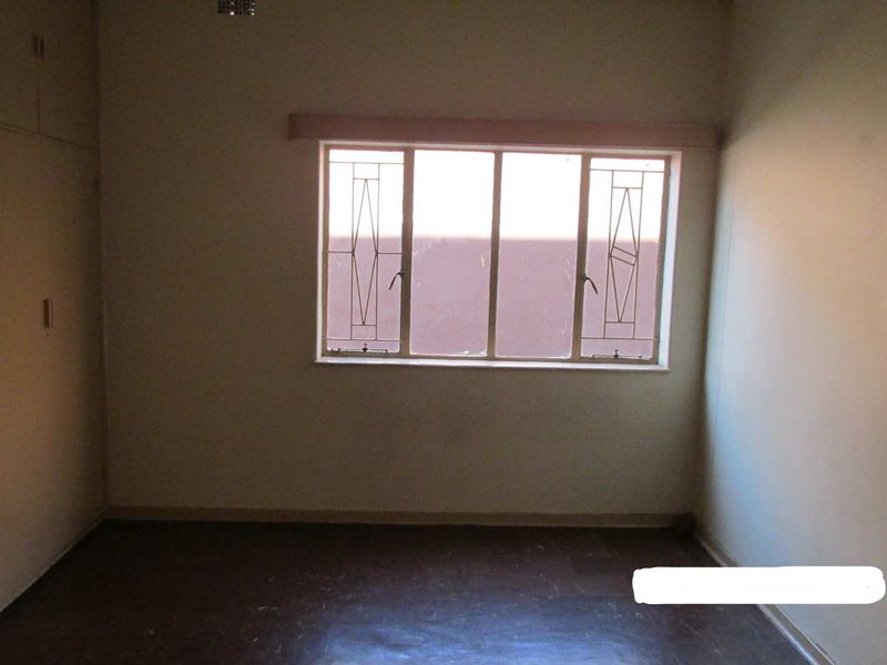 An empty bedroom featuring built-in cupboards and security bars on the window, requiring cosmetic updates to improve its overall condition.