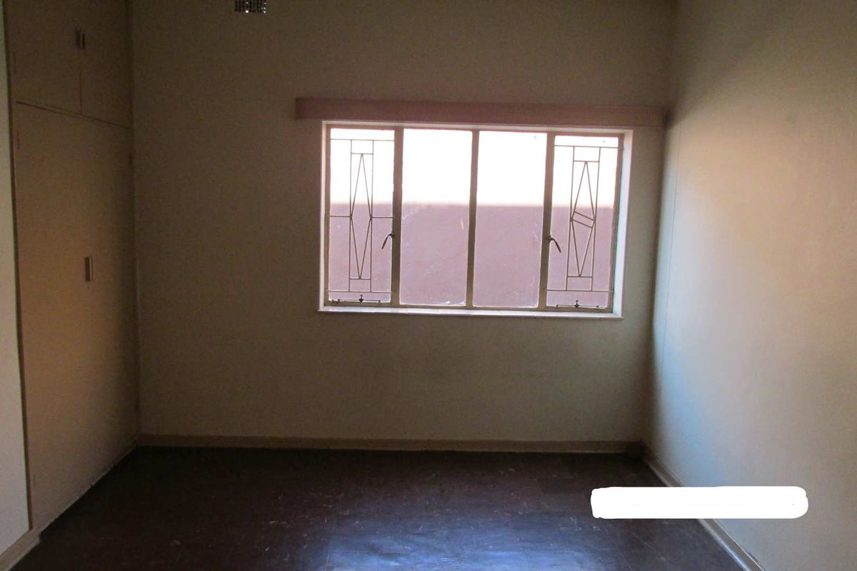 An empty bedroom featuring built-in cupboards and security bars on the window, requiring cosmetic updates to improve its overall condition.