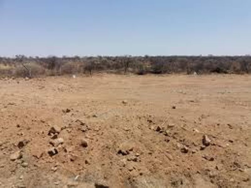 A wide-angle view of a vacant, undeveloped plot of land with dry, cleared terrain and sparse vegetation in the background.