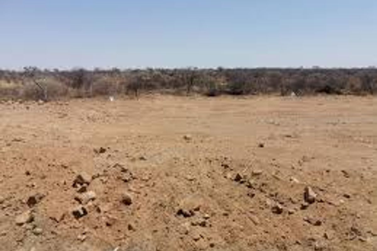 A wide-angle view of a vacant, undeveloped plot of land with dry, cleared terrain and sparse vegetation in the background.