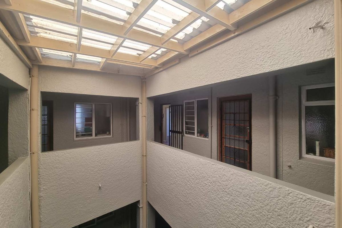 An open-air central courtyard or light well featuring a timber pergola with translucent roofing, providing access to multiple apartment entry points.