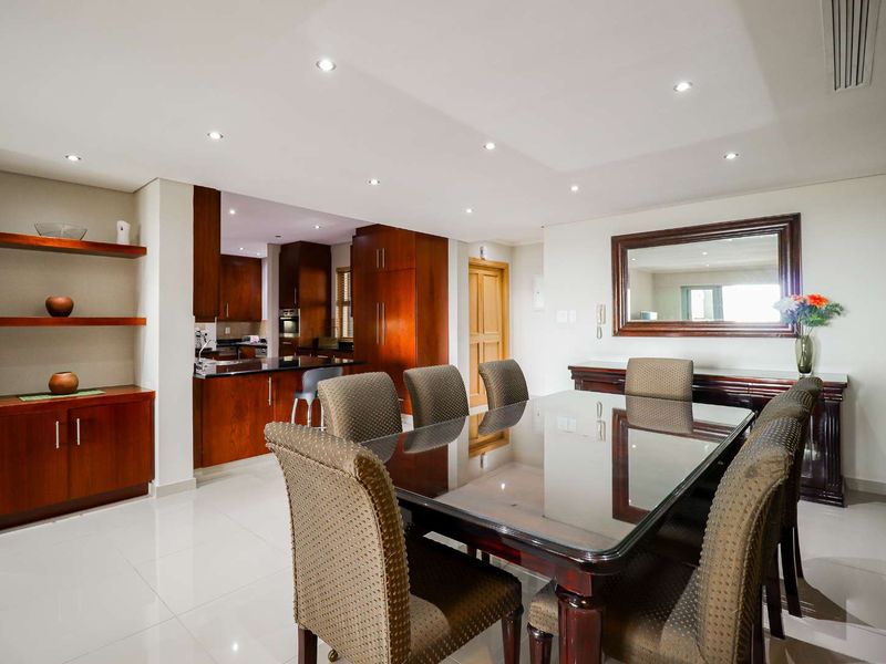 Open plan dining and kitchen area featuring polished tile flooring, recessed lighting, and warm-toned wooden cabinetry with integrated appliances.