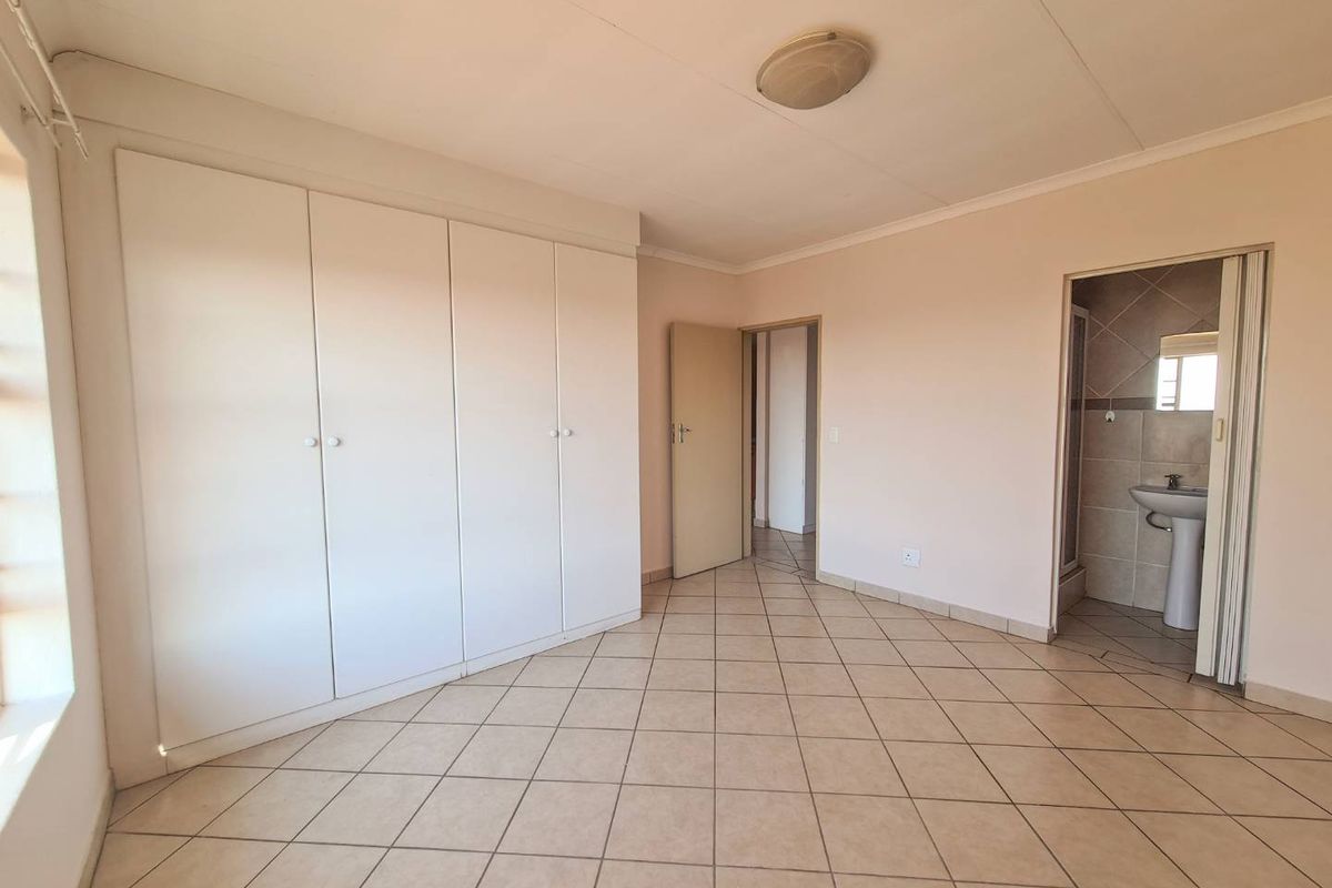 A spacious, empty bedroom featuring tiled flooring, built-in cupboards, and direct access to an en-suite bathroom.